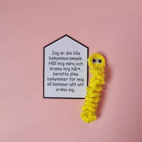 En liten virkad mask i gul färg med en lapp fäst vid sig